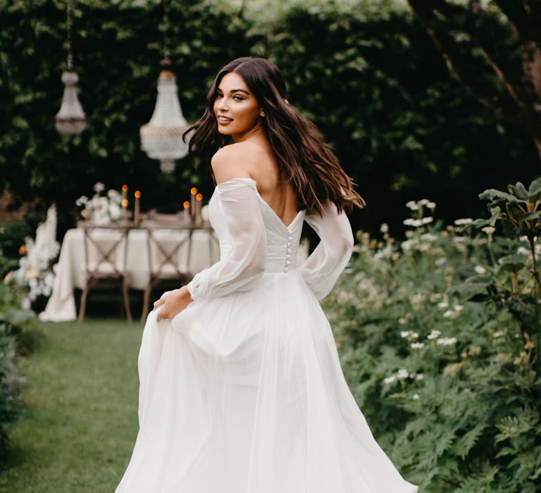 Bride in a chiffon Suzanne Neville bridal gown with ruched fabric and button back detail running through the gardens at Barnsley House