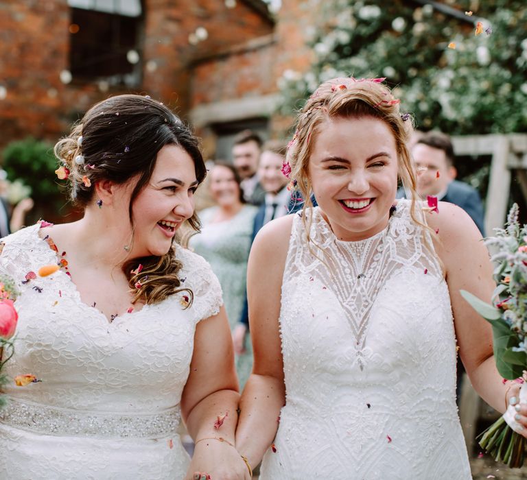 Brides laugh and walk through confetti together on their wedding day