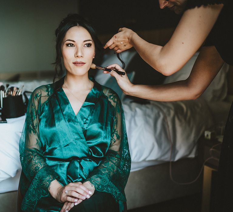 East Asian bride has her hair done on her wedding day as she wears deep green silk dressing gown