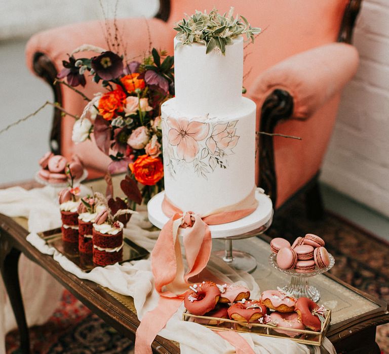 hand painted wedding cake with pink floral design and ribbon and foliage hoop cake topper 