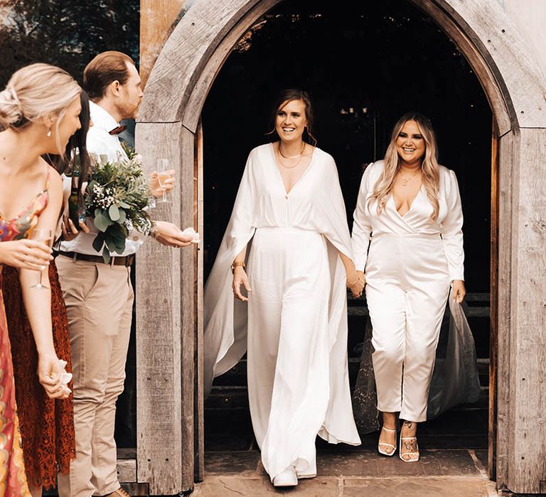 Brides leave wedding ceremony through wooden arched doorway