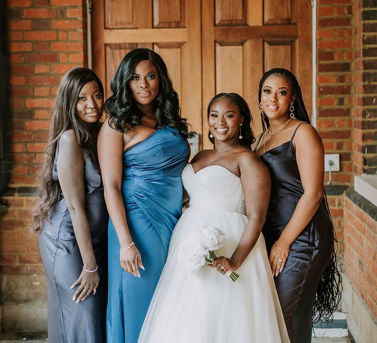 Bride in white wedding dress surrounded by three bridesmaids each in different full length blue gowns