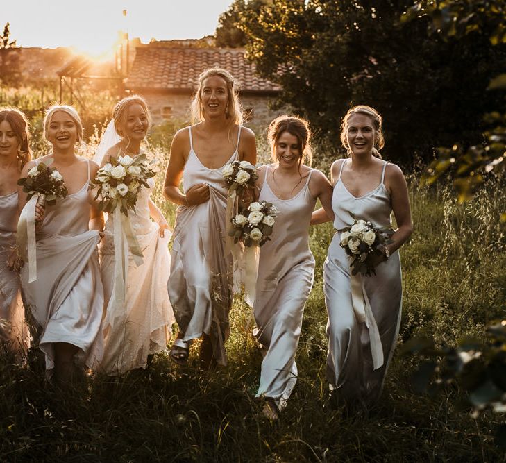 golden hour portrait of the bride party walking through the fields with bridesmaids in silver satin slip dresses 