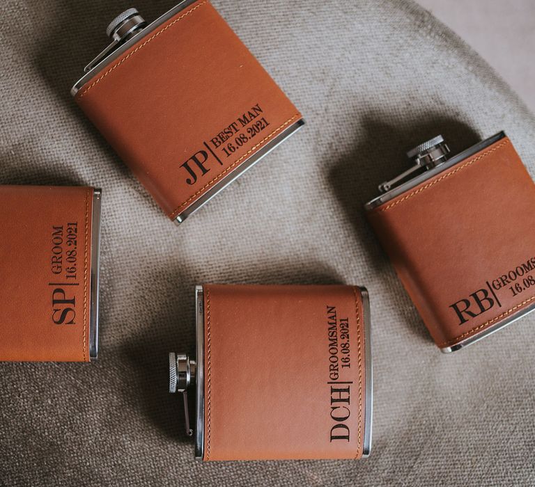 Four orange leather hip flasks with personalised initials on chair at Tythe Barn wedding with barn wedding flowers