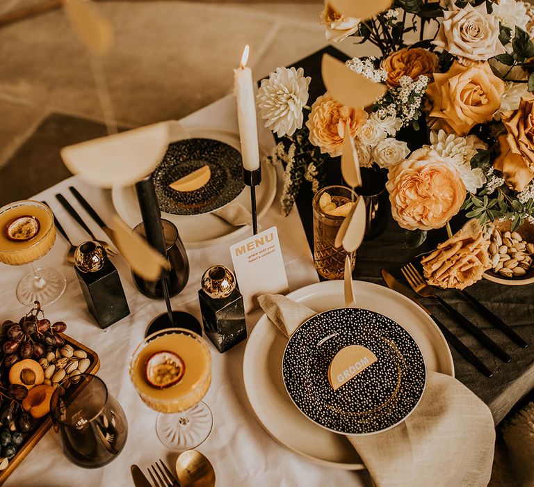 Place setting with beige charger plate black tableware and orange and yellow flowers 