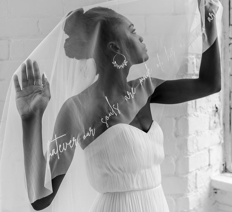 Black bride in a strapless wedding dress holding her personalised veil out showing off the quote 'whatever ours souls are made of his and mine are the same'