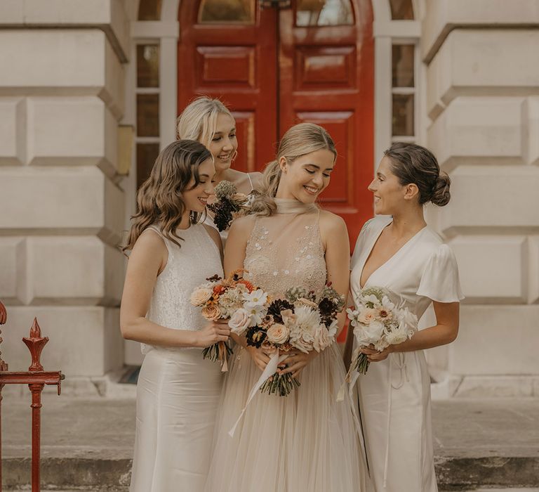 Bridal party portrait standing on some steps with a red door in the background holding orange and white autumn bouquets 