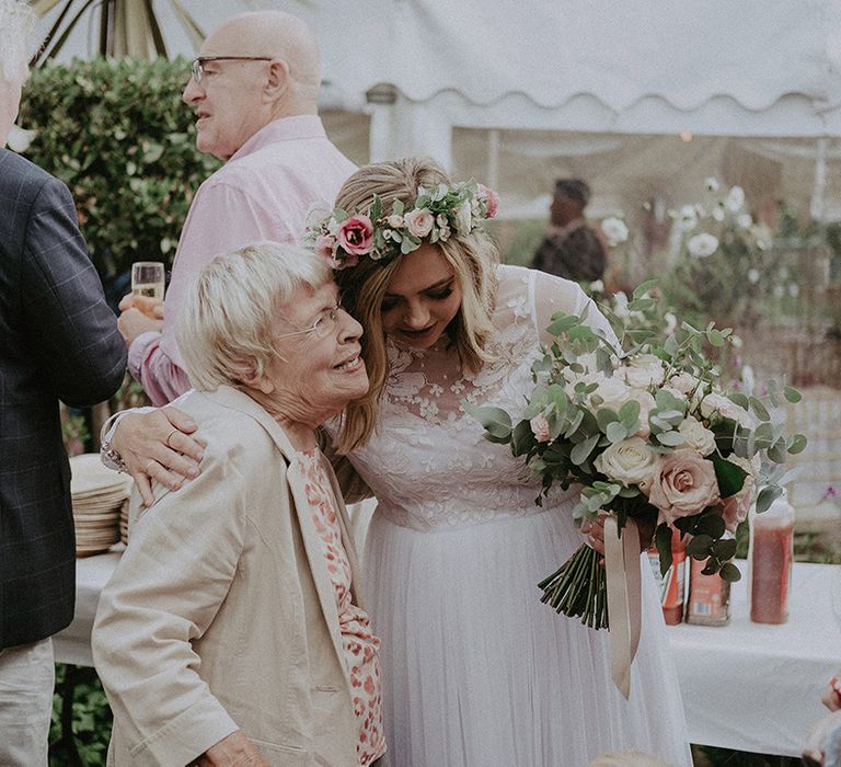 Bride in a long sleeve wedding dress and flower crown hugging her nan at her back garden wedding 