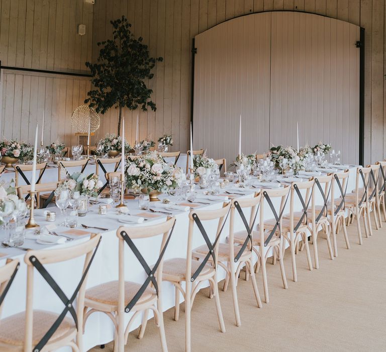 Long wooden tables with florals, white dinner candles and wooden chairs in large whitewashed barn at Primrose Hill Farm wedding