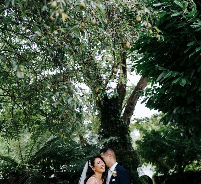 Bubbly couple laughing in forest setting while Bride holds her Pink King protea and rose wedding bouquet 