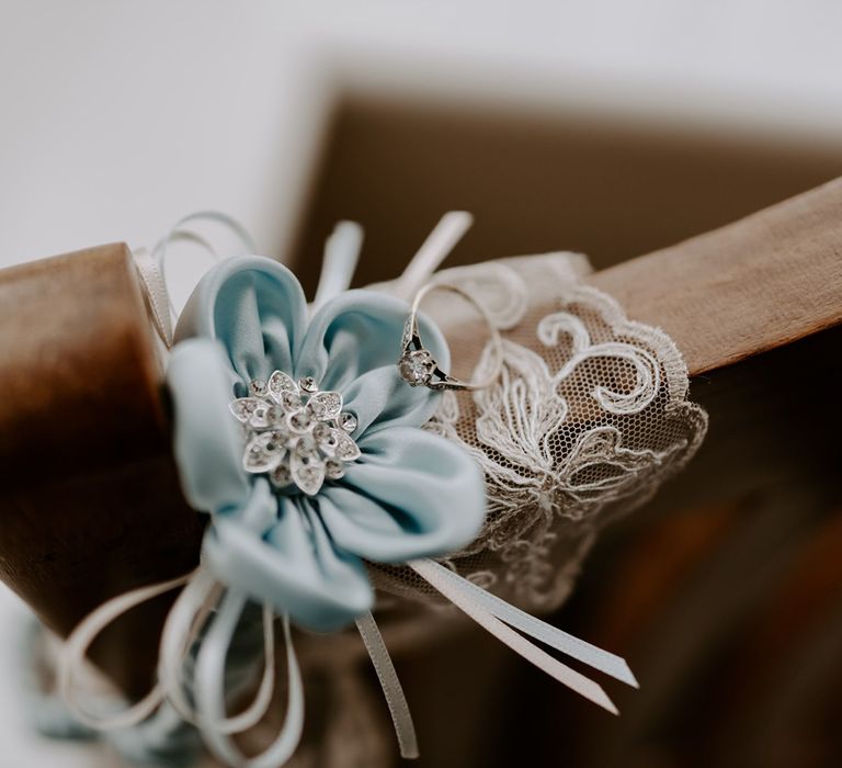 Blue silk flower with silver centre and diamond wedding ring resting on wooden chair before DIY garden wedding in Bedfordshire