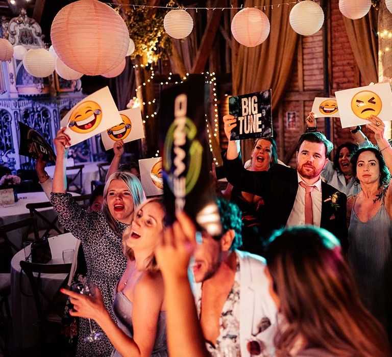 Wedding guests holding up 'tune' and emoji signs to the bride and groom on the decks 