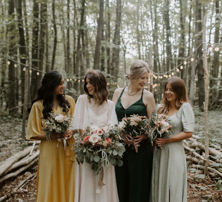 Bride stands with her wedding party who all wear different style and coloured gowns whilst holding floral bouquets