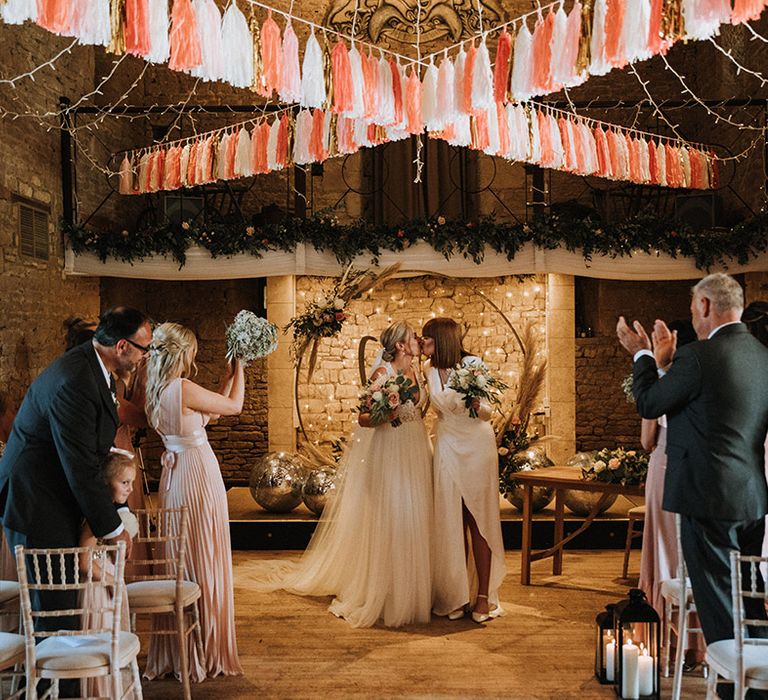 Brides kiss during ceremony with fairy light backdrop and tassel diy decor