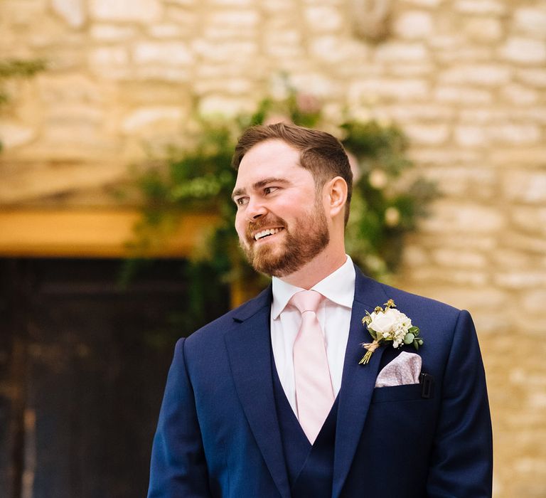 Groom in a navy blue three piece suit with white shirt, pink tie and white rose buttonhole flower 