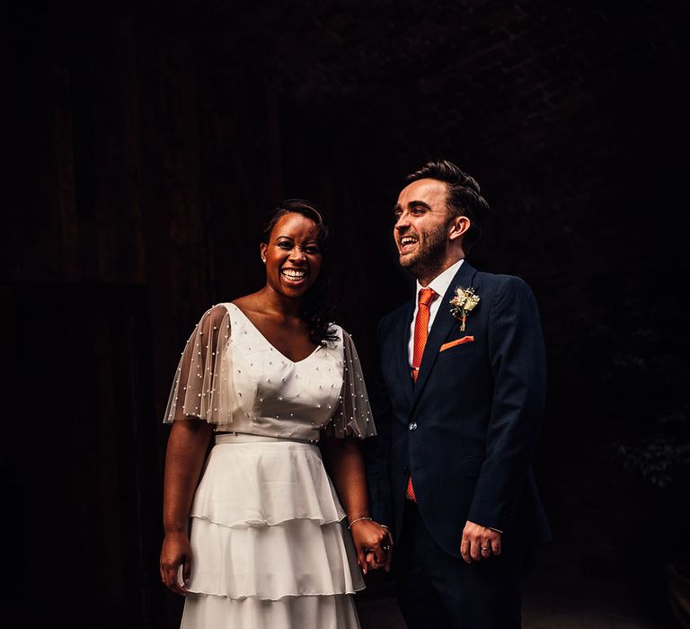 Groom in a navy suit with orange tie holding hands with his Black bride in bridal separates 