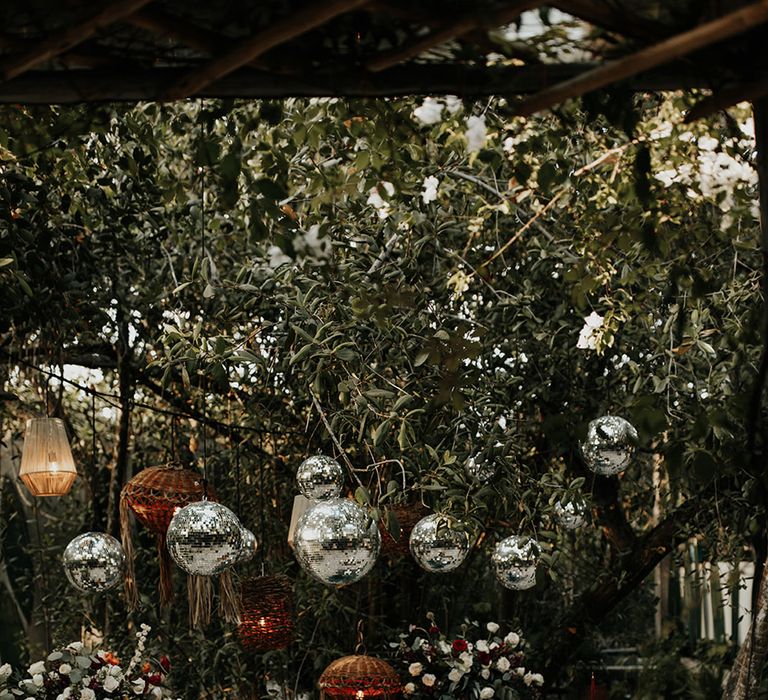 Jungle settings for the wedding reception with wooden top table and candle lanterns and disco balls for wedding decor