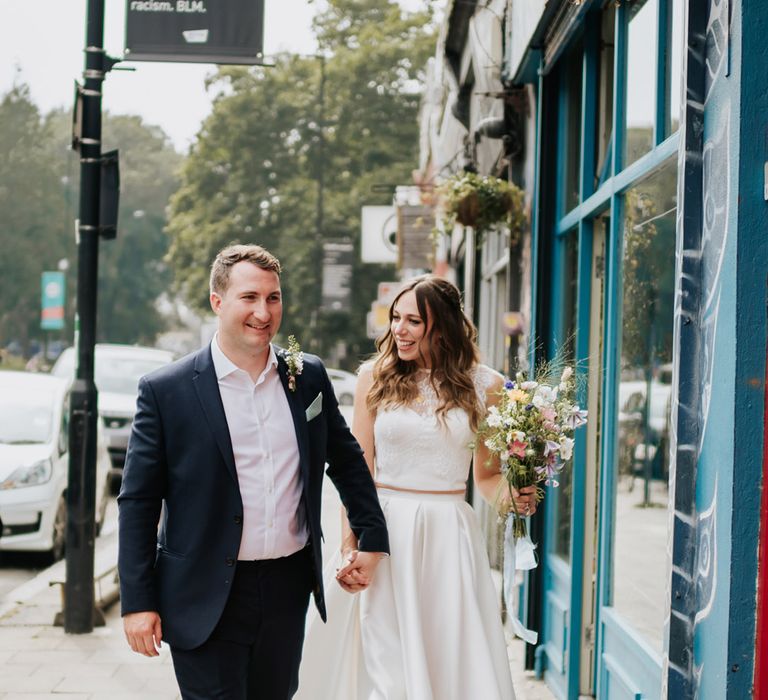 Bride and groom walking the streets with bride in high low pleated wedding skirt and electric blue wedding shoes 