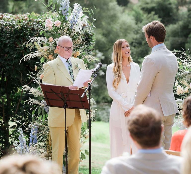 Bride at groom at their outdoor summer wedding with pastel flower displays and bespoke ceremony