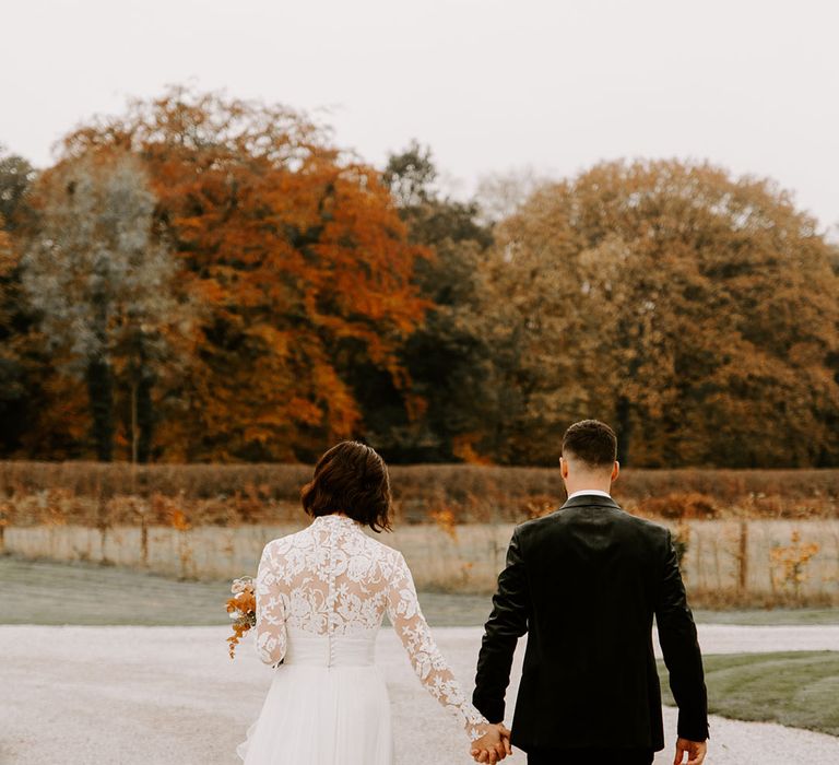 Bride in lace back buttoned wedding dress holds hands with groom in black jacket