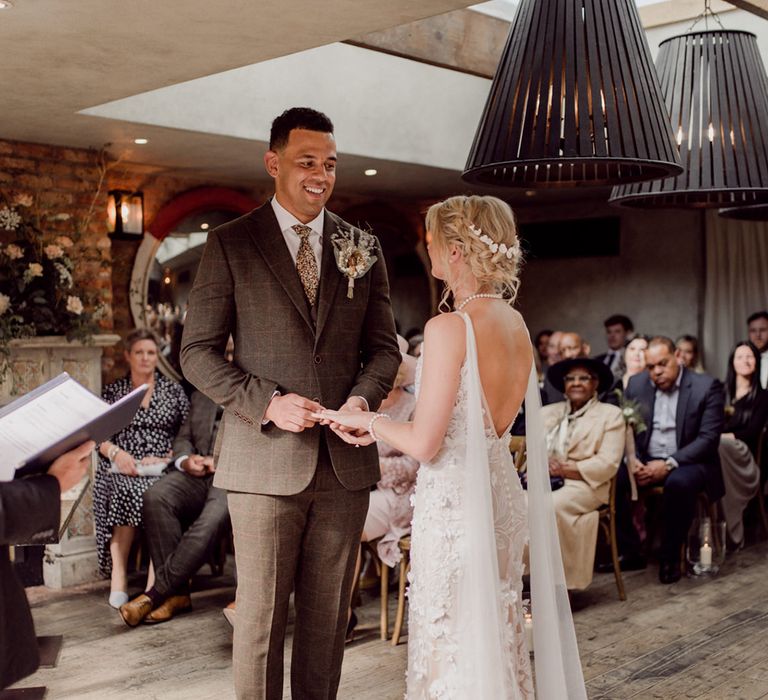 Bride in 3D lace floral wedding dress with pearl necklace with groom in checkered brown suit and patterned tie