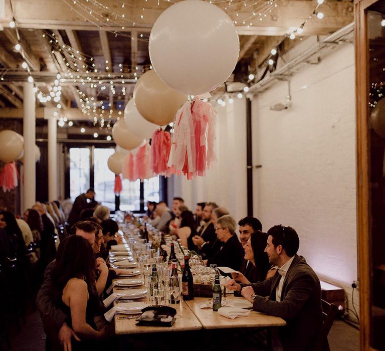 Large white balloons with pink tissue paper tassels and fairy lights decorate the wedding reception at industrial wedding venue 