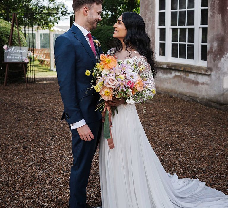 Bride and groom smile and look into each other's eyes as she holds spring wedding bouquet with giant poppy 