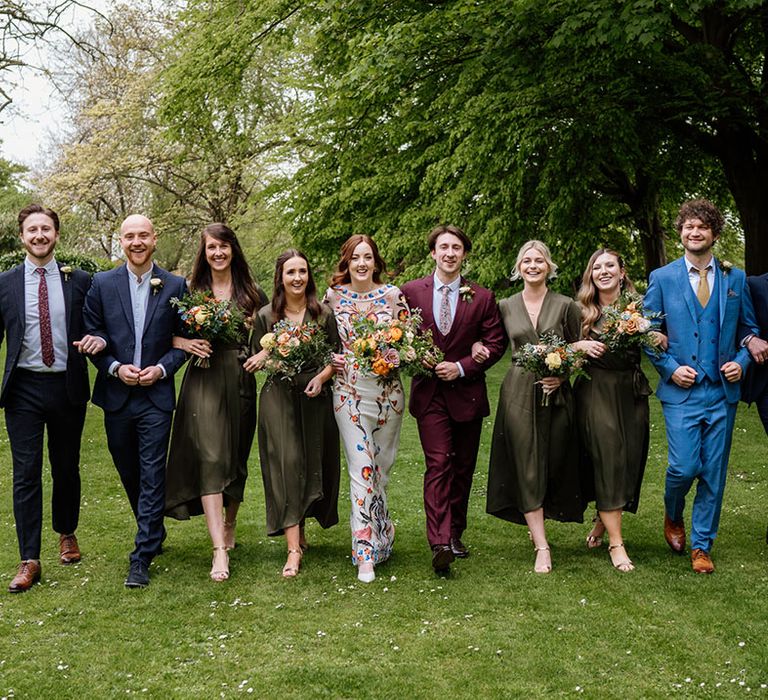 Wedding party wearing different coloured suits, a colourful wedding dress and bridesmaids in matching green wrap dress