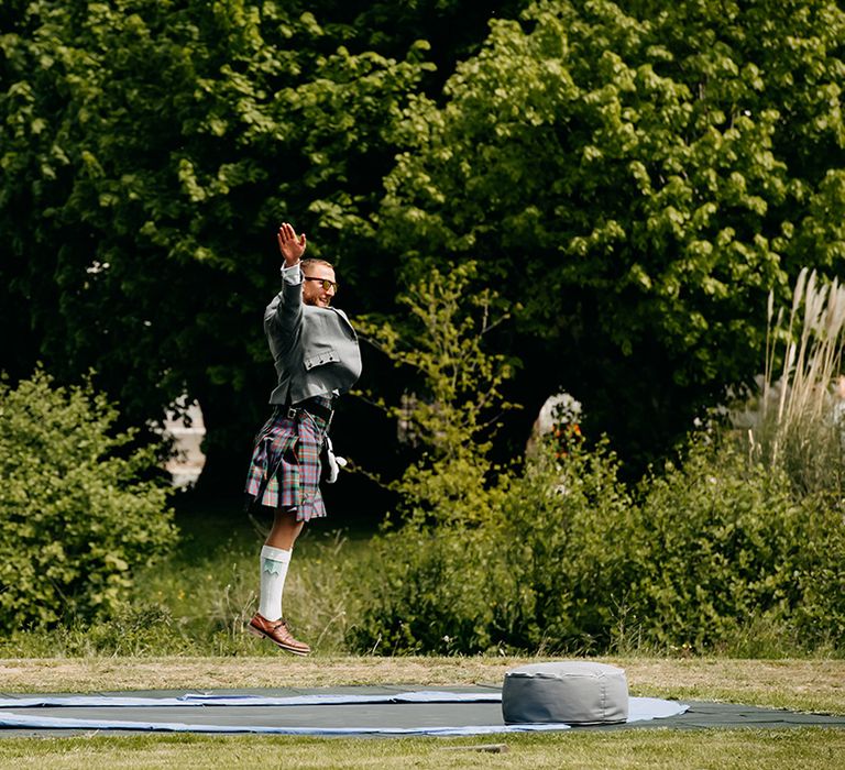 Wedding guest wearing a kilt has fun on a trampoline 