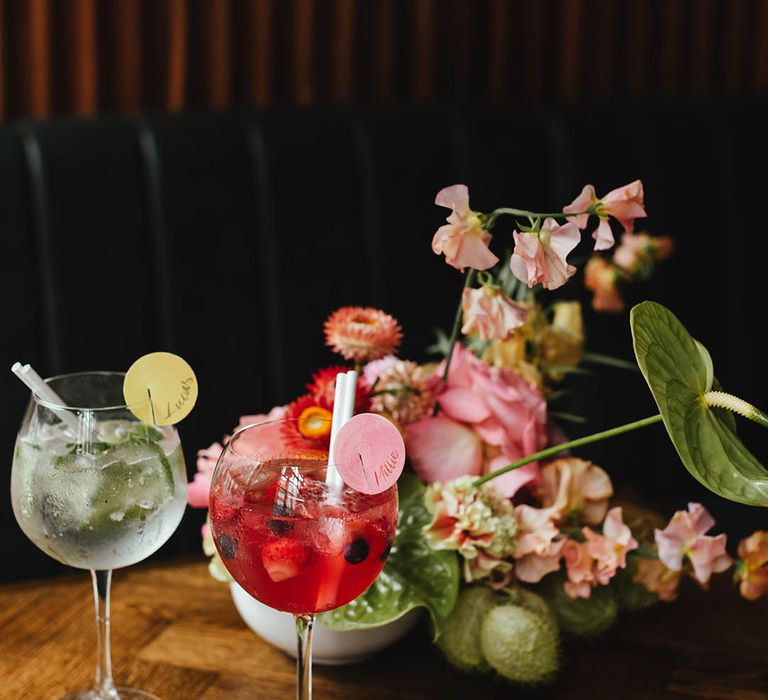 Gin cocktails in balloon glasses with name glass tags and pink and green wedding flowers 