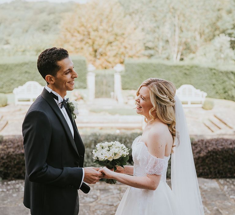 Bride and groom hold hands with groom in black tie and bride in off the shoulder wedding dress