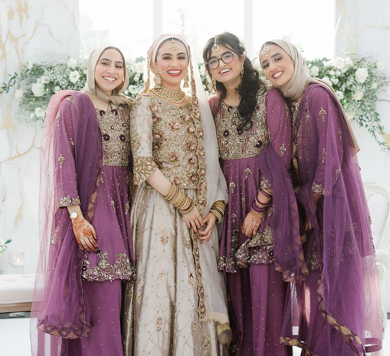 Bride stands with her bridesmaids who wear purple saree's complete with gold embellishment 