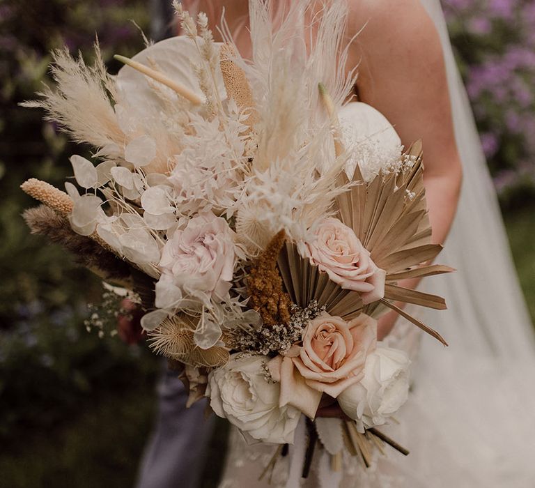 Bride holds muted tone dried floral bouquet filled with roses, anthuriums and pampas grass