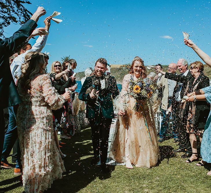 Bride & groom walk through confetti after outdoor wedding ceremony on the beach front in Cornwall 