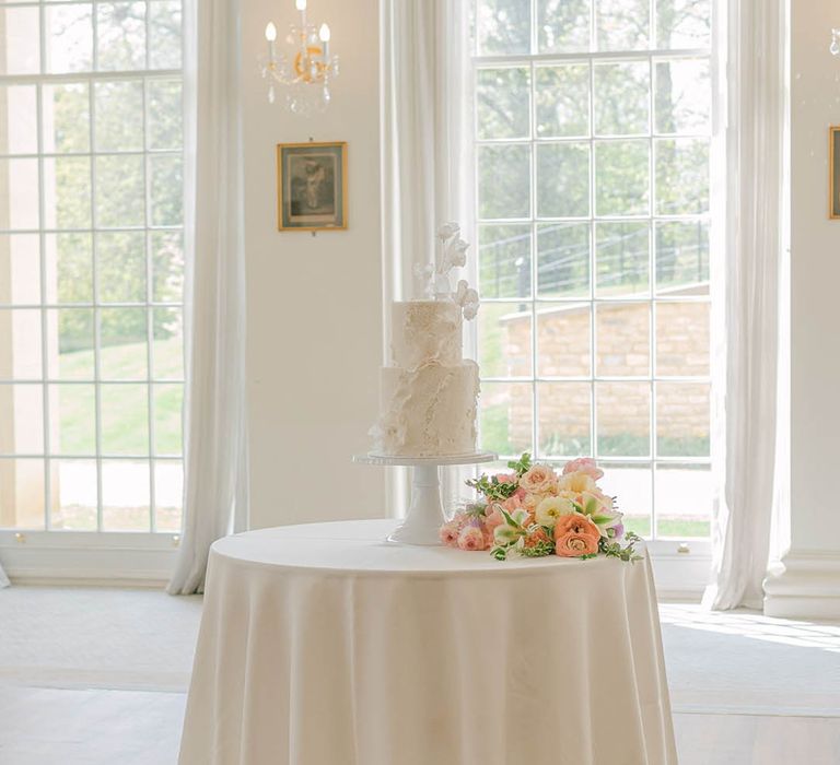 White two tier wedding cake with texture detail on a white table with the pretty pink and purple pastel bouquet 