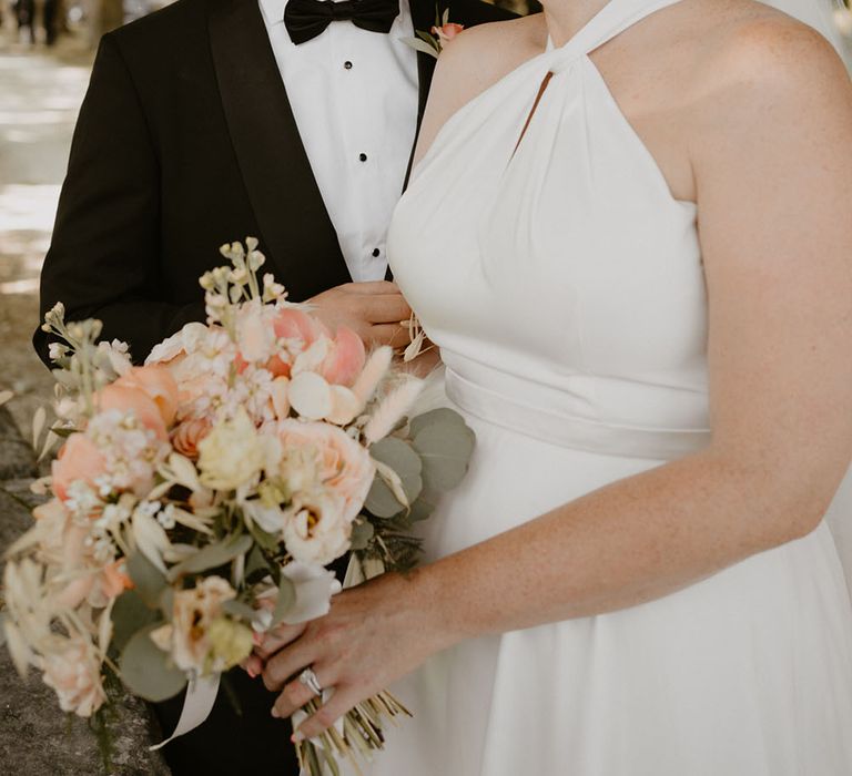 Bride wears halterneck Halfpenny London wedding dress whilst looking lovingly at her groom in black tie 