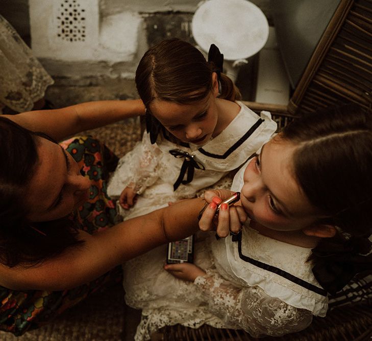 Flower girls wear lace dresses complete with black ribbon as they have red lipstick applied on the morning of wedding day