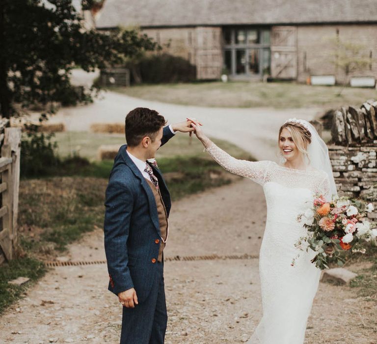 Bride with braided hair and headband in lace wedding dress dances with the groom in a blue suit 