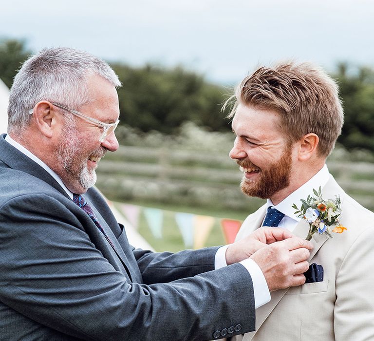 Father of the groom helps the groom with his buttonhole for the rustic wedding at Deepdale Farm 