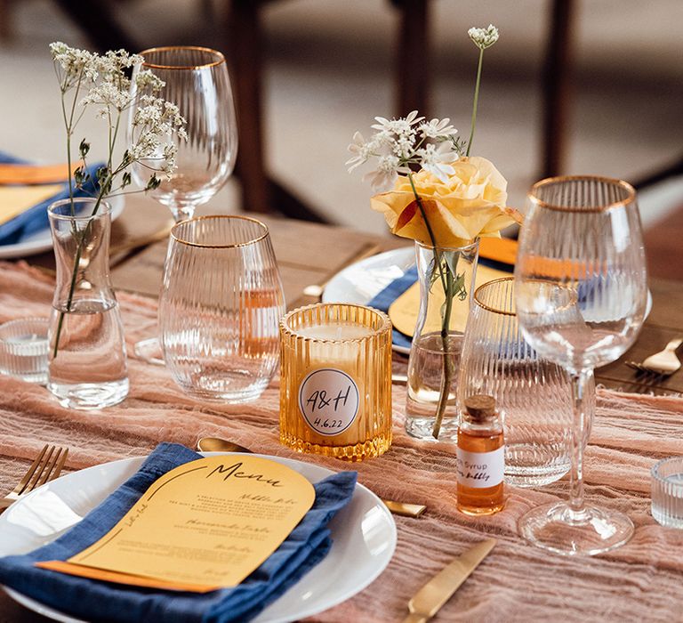 Fluted glassware with a gold rim, orange and blue colour scheme with syrup favours and personalised candles 