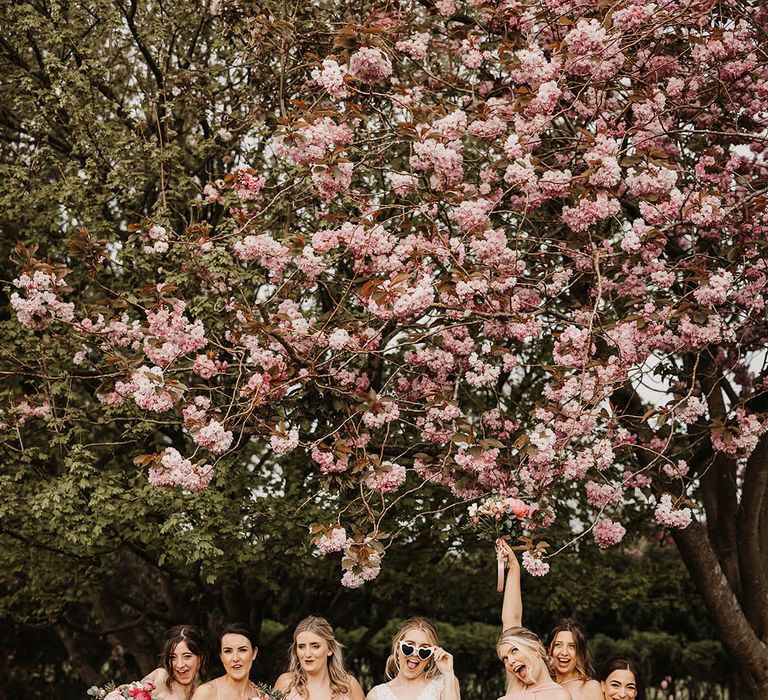 Bridesmaids in pink dresses with the bride in a lace wedding dress and retro sunglasses under a pink blossom tree