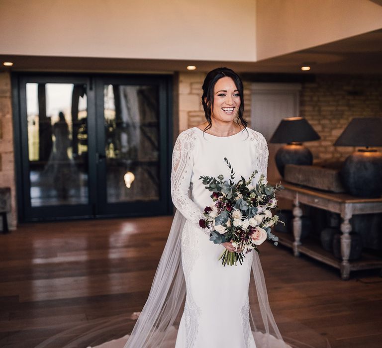 Bride holding a wintery bouquet of white and red flowers in an Atelier Pronovias long sleeve lace and beaded wedding dress 