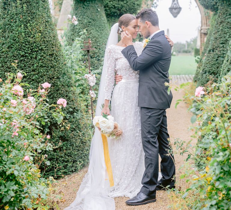 The groom in traditional black tie cups the bride's face holding a yellow and white flower bouquet for their outdoor wedding 