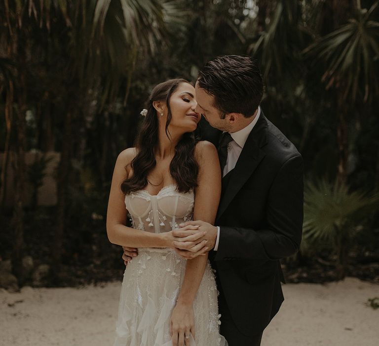 Bride wearing corset styled embellished wedding dress stands beside her groom outdoors 