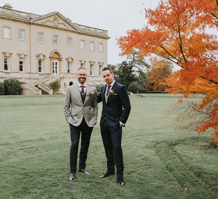 Grooms pose together in front of their country house wedding venue 