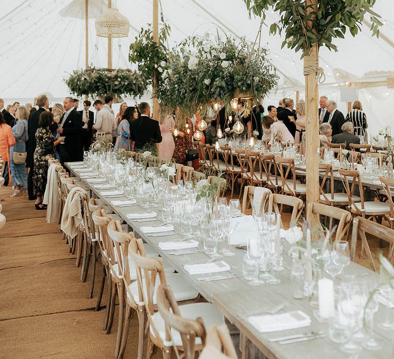 Marquee wedding reception complete with wooden banquet tables, hanging green foliage installations and fairy lights