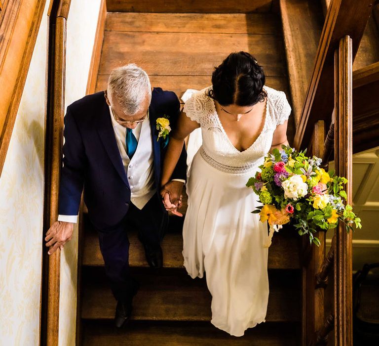 Bride walks down the stairs with her father on the morning of her wedding day before outdoor ceremony 