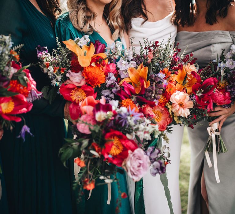 Bright and colourful bride and bridesmaid bouquets with pink, red, orange, and purple flowers including lilies and wax flowers