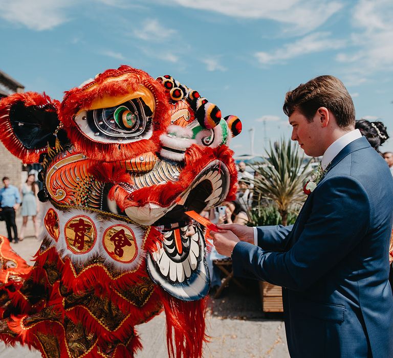 Groom places red envelope in the mouth of dragon during Lion Troupe Dance 