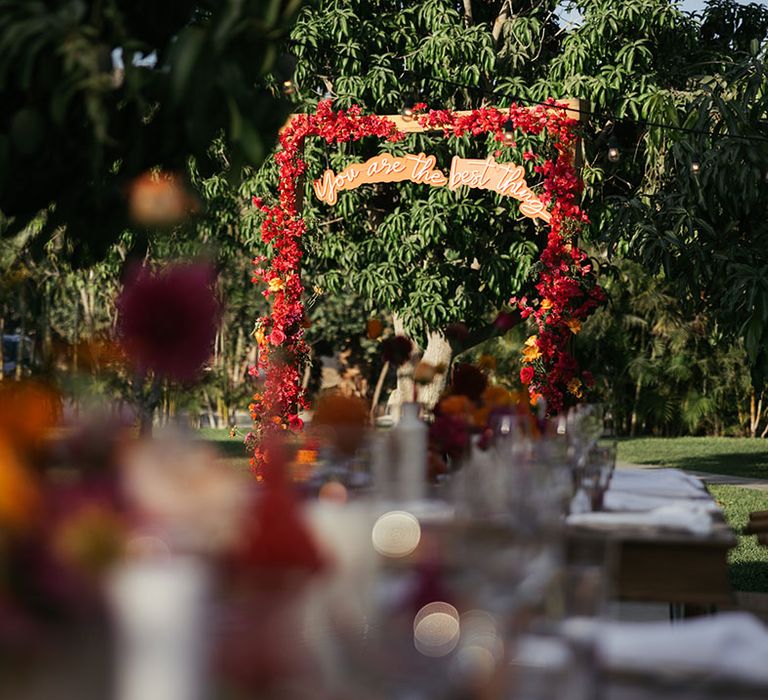 Outdoor floral arch complete with red blooms and personalised sign hanging to the middle 